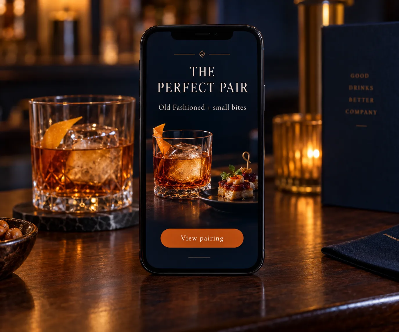 A phone standing on a bar top beside an Old Fashioned, showing a promoted pairing, The Perfect Pair, Old Fashioned and small bites, with a View pairing button.